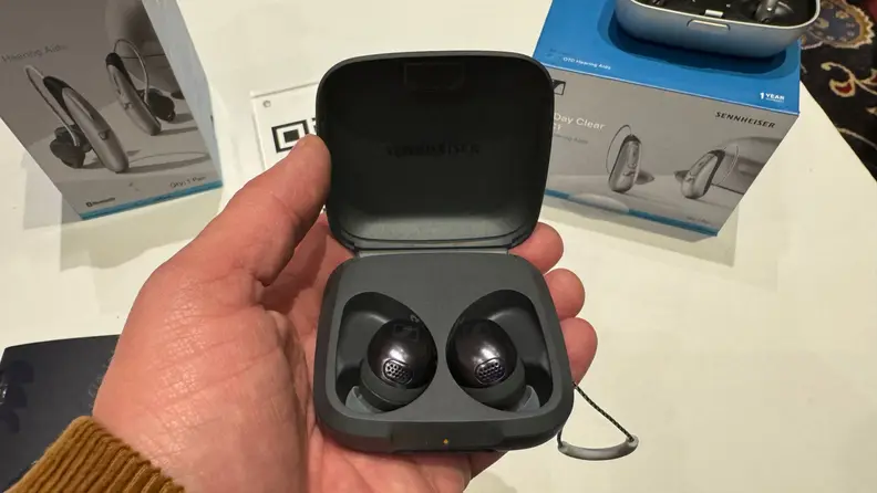 A hand holds a pair of Sennheiser Momentum Sport in their gray carrying case.