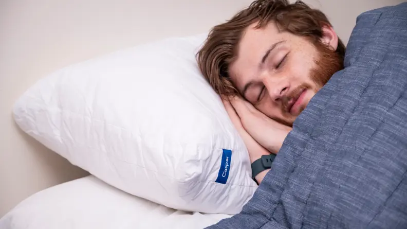 A man sleeps on the Casper Original Pillow under a blue blanket