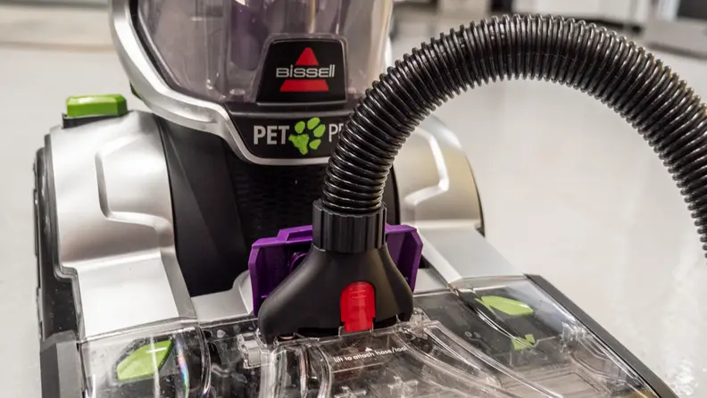 A hose is plugged into the front of a carpet cleaner