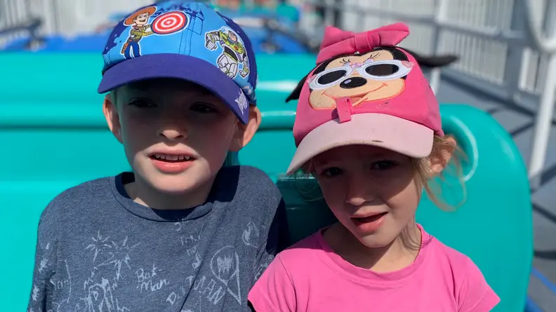 A young boy wearing a Toy Story baseball cap sitting next to a young girl wearing a pink mini mouse hat