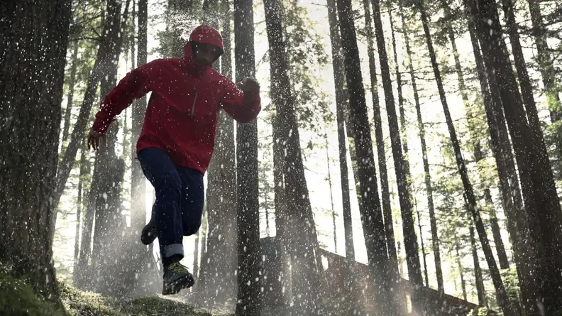 Man running in woods wearing red Gore-Tex jacket.