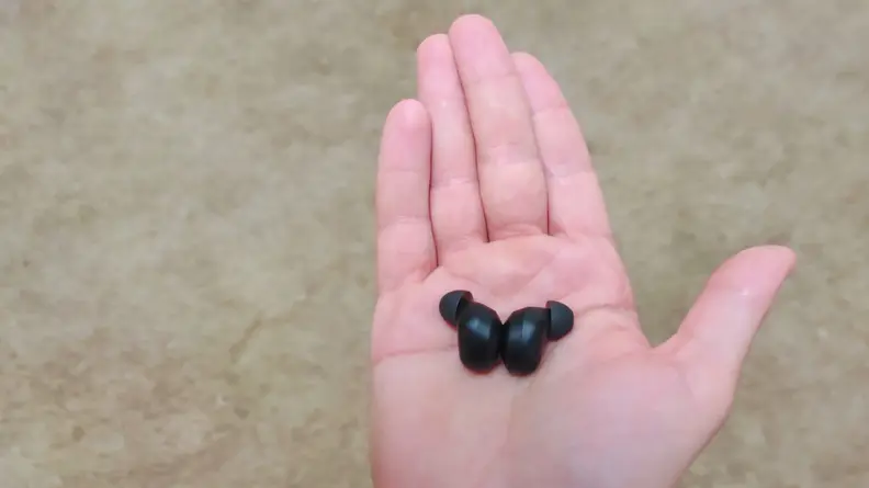 The all black Raycons sitting in the palm of a hand, with their exteriors facing each other.