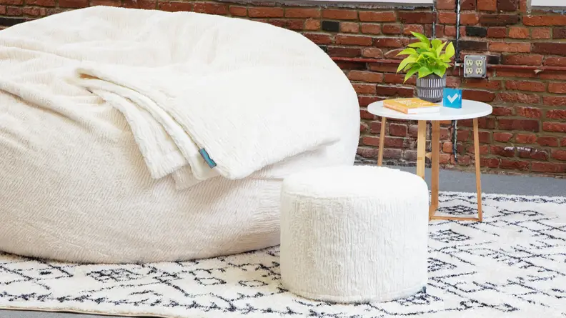 A squattoman sitting next to one of Lovesac’s Sacs.