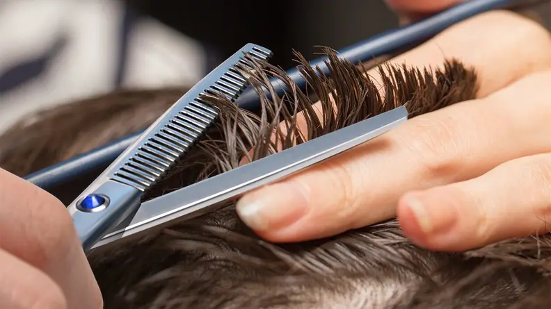 A photo of a man using thinning shears on his hair.
