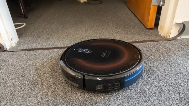 A Eufy Edge vacuum robot on a carpet in between a door.