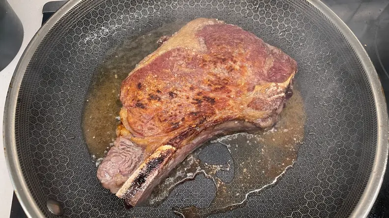 Ribeye steak searing inside of oily skillet pan.
