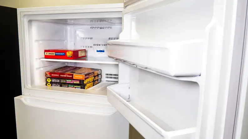 A shot of the Frigidaire FFTR1814VW top-freezer refrigerator's freezer door and interior. The interior has some frozen pizza boxes stacked up inside, for scale.