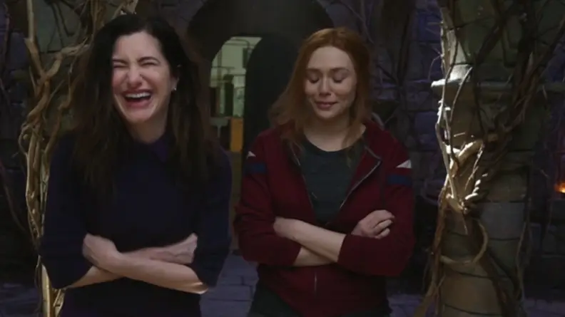 A still from the Assembled series featuring Kathryn Hahn and Elizabeth Olsen in costume, breaking character by laughing.