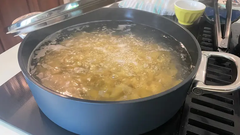 A shallow casserole pan boiling water and pasta.