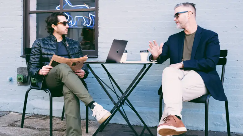 Two individuals siting down having a conversation over coffee.
