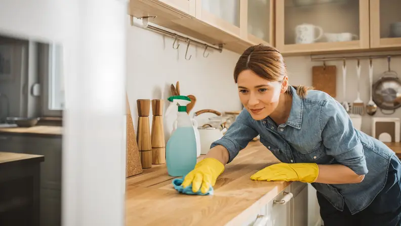 A woman wipes down a kitchen counter.