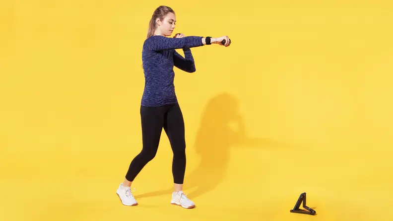 Person standing in boxer stance with legs spread apart and fisted hand extended forward in front of phone stand on ground.