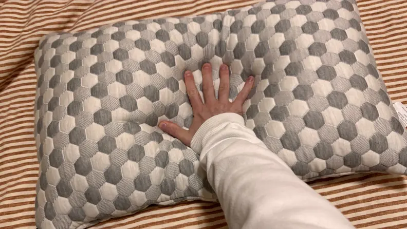 Grey and white hive pattern on Layla Sleep Kapok Pillow with a hand pushing down the middle to show softness.