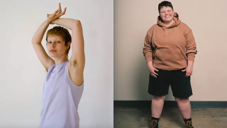 One person wearing a tank top with their arms above their head next to a person wearing shorts and a sweatshirt standing in front of a wall and smiling.