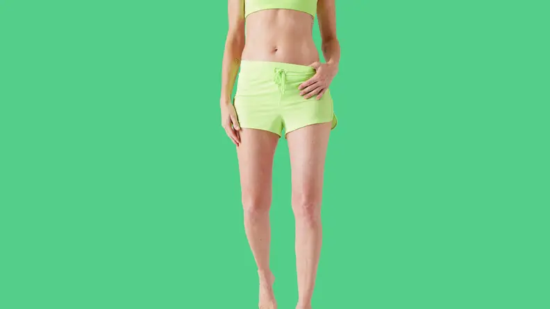 white woman wearing green swim shorts on green background