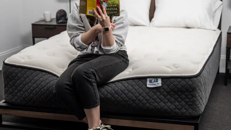 woman seated on edge of mattress with book