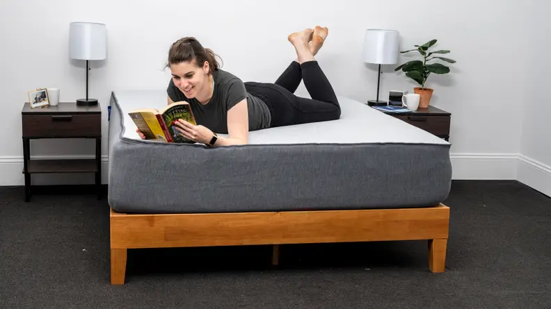 a woman lies on her stomach on the Casper Select and reads