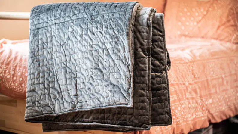 the gravity blanket sits draped over a bed railing