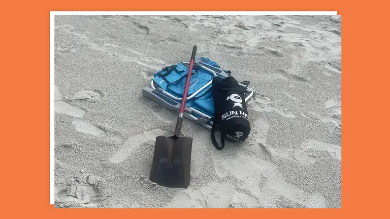 Tent, shovel and beach chair sit together on sandy beach.
