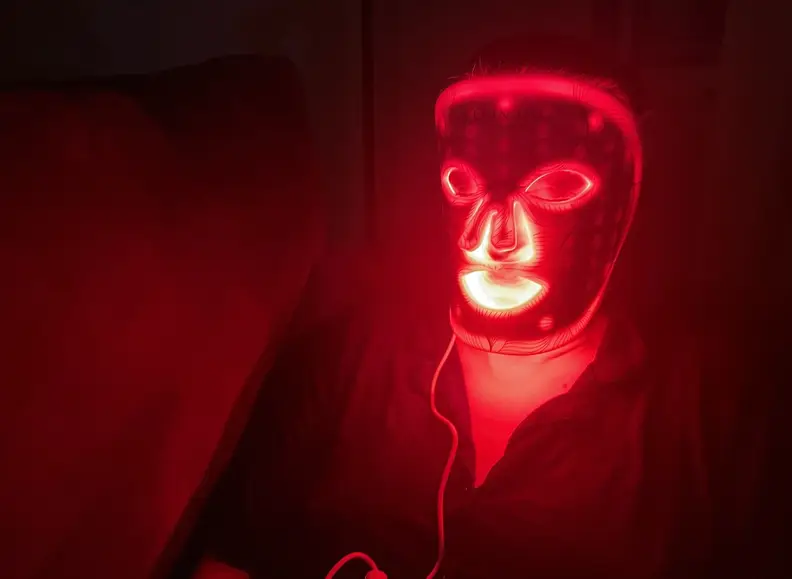Person wears a red light LED mask at night and glows red.