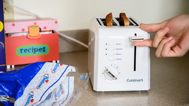 Person adjusting the lever on the Cuisinart 2-slice toaster, filled with two slices of bread.