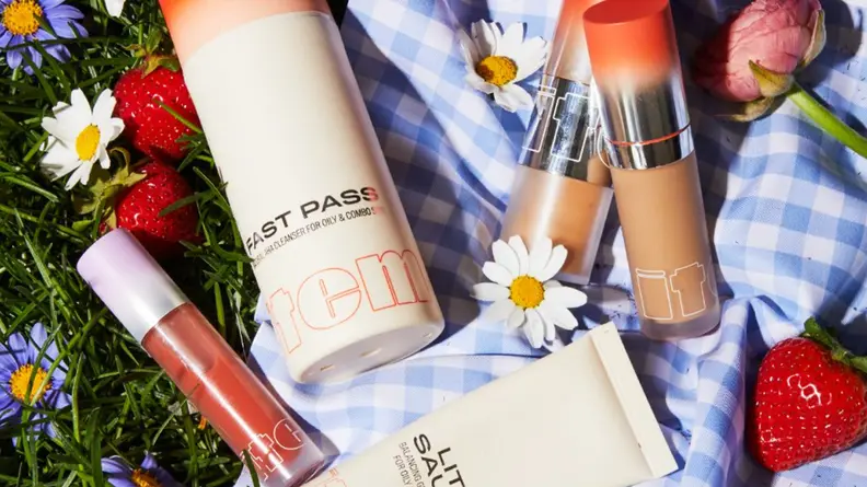 A smattering of Item Beauty products laying on a blue and white checkered blanket.