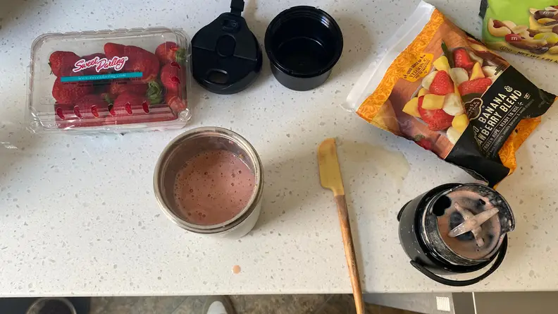 Fresh strawberries, frozen fruits, a smoothie blend and the base to the NutriBullet Flip all laid on the counter.