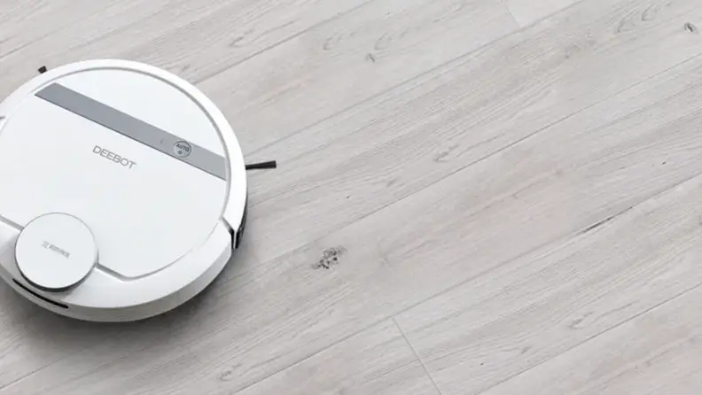 A white robot vacuum in the corner on a gray floor
