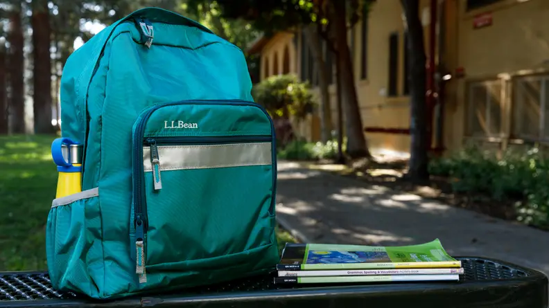 A teal green L.L. Bean backpack on a bench.