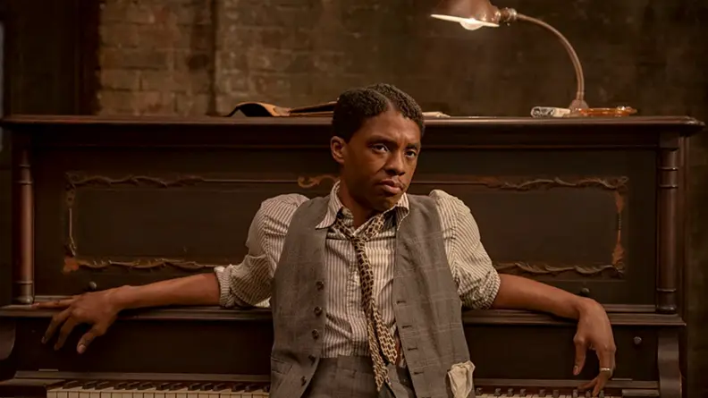 A still from the film Ma Rainey's Black Bottom with actor Chadwick Boseman leaning against a piano