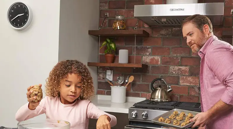 A father and daughter bake cookies together in the kitchen with the Echo Wall Clock in the background.