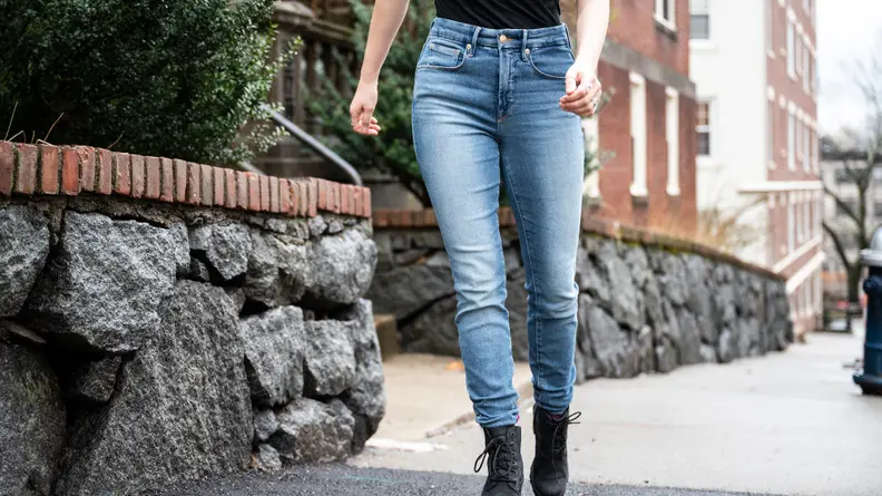 A woman walking down the street in a black shirt and Good American skinny jeans