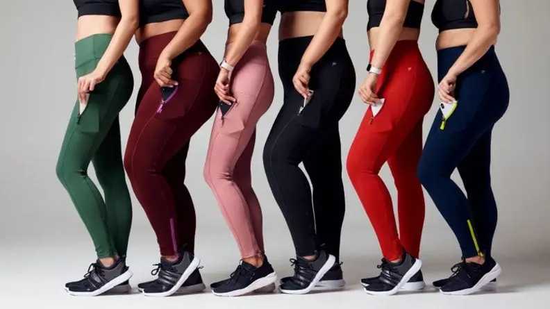 Six women in leggings standing sideways in a line, putting phones in their legging pockets.