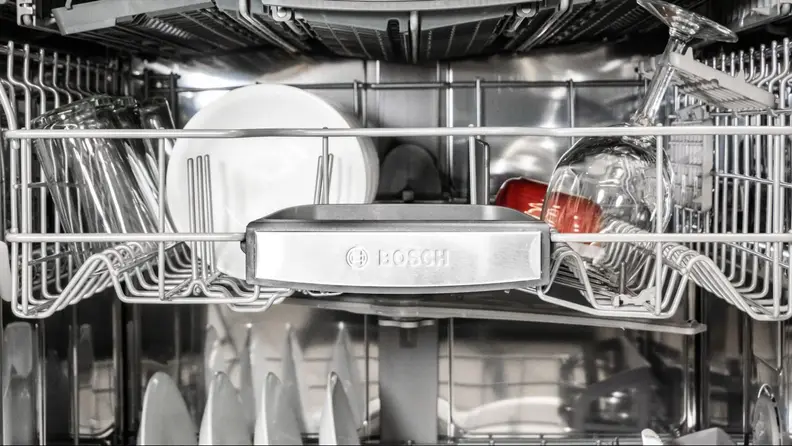A close-up of the Bosch SHP78CM5N 800 Series dishwasher's top rack, focusing on the Bosch-branded handle. It's stocked with clean dishes.