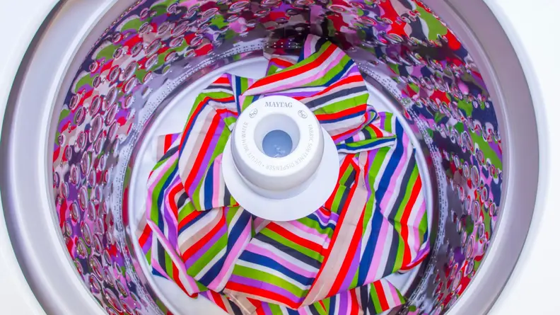 Brightly colored clothing garment inside of spin drum of washer machine.