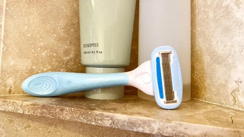 The Solimo 5-Blade Razor for Women laying on a shower shelf with body wash behind it.