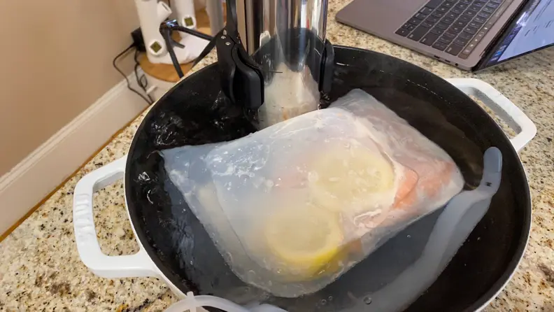 In a large Dutch oven filled with water, a salmon fillet is being cooked in a sous vide silicone bag monitored by a sous vide immersion circulator.