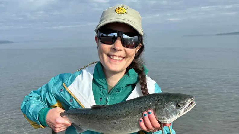 A woman holding up a freshly caught fish from the ocean.