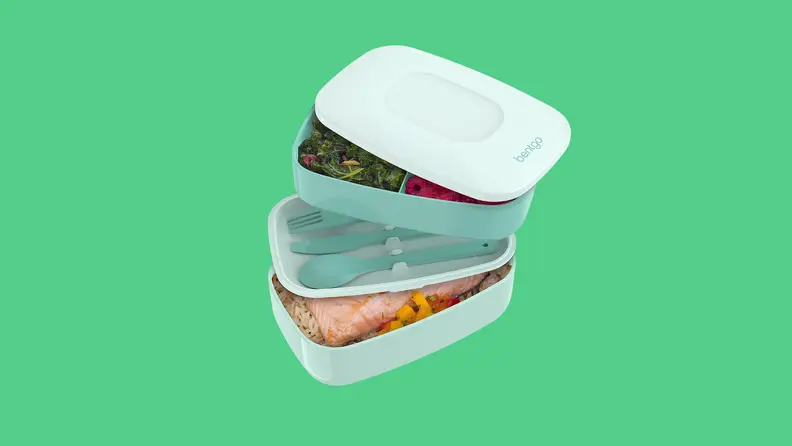 A light teal Bentgo lunchbox opened in a stair-like fashion to reveal two compartments full of food and plastic utensils.