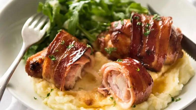 Bacon-wrapped chicken on a bed of mashed potatoes and salad