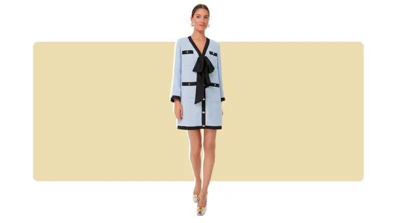 A light blue tweed dress with black piping, gold buttons, and a loose black bow at the center.