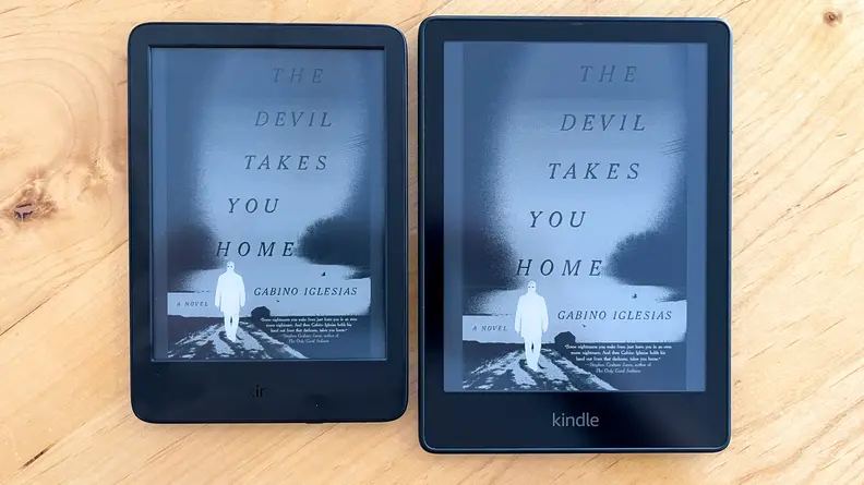 A base model Kindle sits on a table next to a larger Kindle Paperwhite.