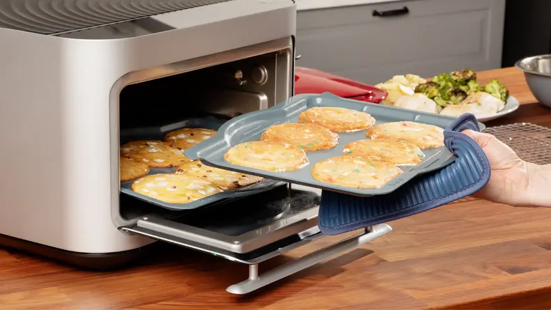 Person removing a tray of colorful cookies from the Brava Glass oven.