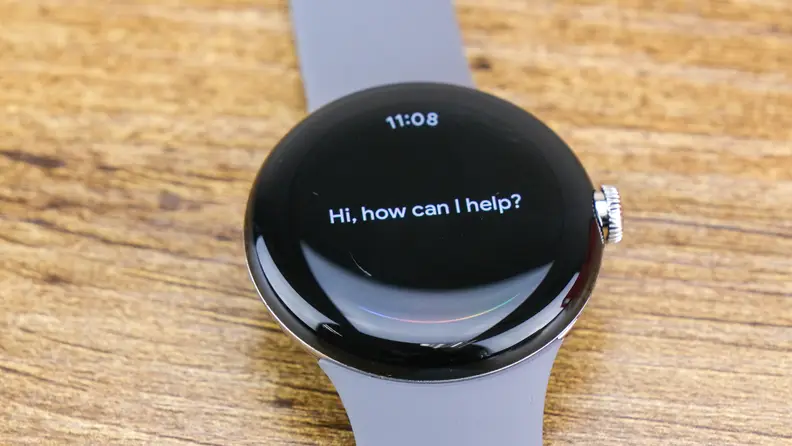 A Google Pixel Watch sits on a counter top displaying the message 'How can I help?'