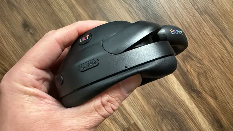 A hand compressing the ear cup padding of the Sony Ult Wear headphones.