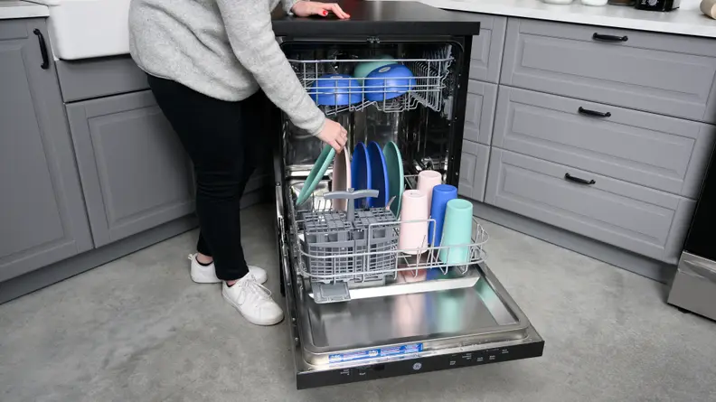 The GE GPT225SSLSS portable dishwasher,open and being filled with colorful pastel dishes.