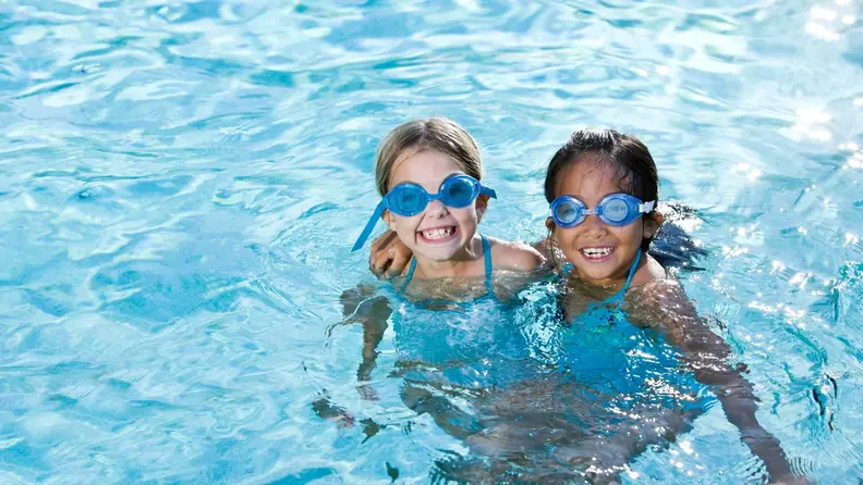 Two girls hug each other and smile in a pool.