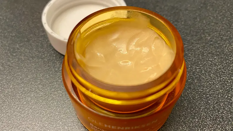 The OleHenriksen Banana Bright Eye Crème sitting on a bathroom vanity with its lid off to expose a orange-tinted cream.
