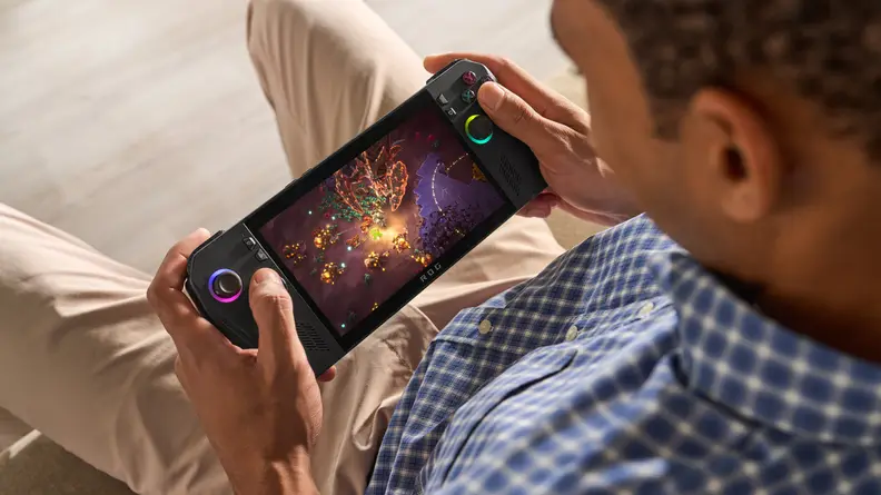 Someone playing a game on the Asus ROG Ally X while sitting on a couch, shot over their shoulder down at the handheld console.