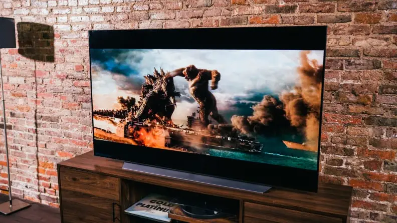 An LG TV showing a scene from Godzilla vs. Kong in front of a brick wall on top of a media console.